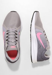 Sneaker sportive grigie con tomaia in rete, dettagli rosa e suola intermedia bianca. Presentano un sistema di allacciatura e suola in gomma testurizzata per una buona aderenza.