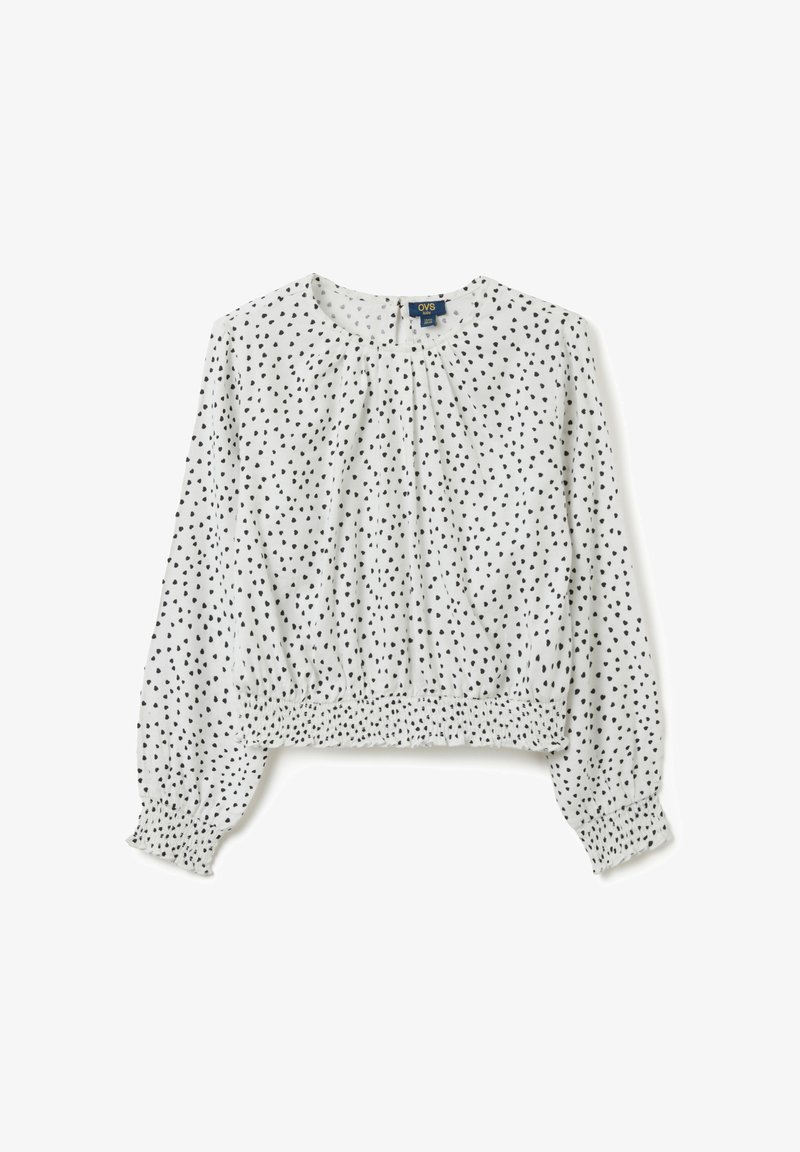 Weiße Kinderbluse mit langen Ärmeln, schwarzem unregelmäßigem Punktmuster, elastischen Bündchen und gerafftem elastischen Saum.