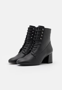 Botas de cuero negras hasta el tobillo con un acabado texturizado. Presentan un cierre de cordones en la parte frontal, ojales metálicos y un tacón grueso. Diseño de punta redonda.