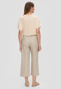 Beige T-shirt met korte mouwen, gecombineerd met lichtbeige cropped broeken, met een gladde textuur en elastische taille. Sandalen zichtbaar.