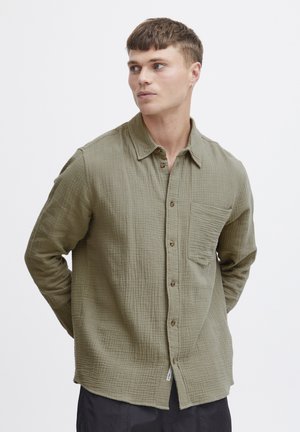 Khaki green button-up shirt made of textured cotton with a pocket, featuring wooden buttons and a relaxed fit.