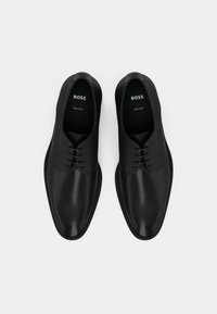 Czarne skórzane buty o gładkim wykończeniu z teksturowanymi akcentami, charakteryzujące się niskim profilem, wiązaniem na sznurowadła oraz logo "BOSS" wewnątrz.