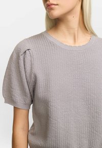 Pulover gri texturat, cu mâneci scurte puffed și decolteu ondulat, realizat dintr-un material tricotat respirabil.