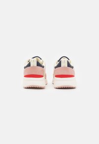 Baskets avec un arrière en suède rose, une tige en tissu bleu marine, des accents crème et un talon rouge, dotées d'une semelle blanche épaisse et d'une semelle extérieure texturée.