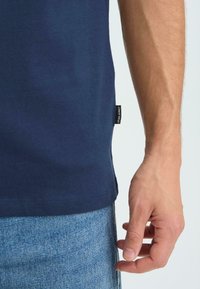 Laivastonsininen puuvillainen t-paita, jossa pyöreä kaulus ja sivusaumalappu. Kangas on sileäpintainen ja rento istuvuus, yhdistetty farkkuihin.