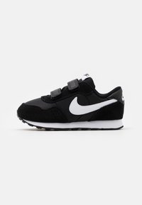 Baskets noires avec un mélange de daim et de matériaux synthétiques, dotées de sangles Velcro, d'un swoosh Nike blanc et d'une semelle intermédiaire blanche.