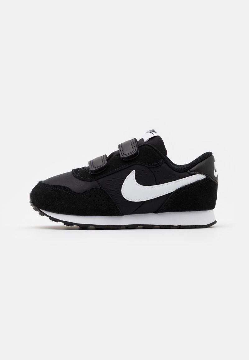 Baskets noires avec un mélange de daim et de matériaux synthétiques, dotées de sangles Velcro, d'un swoosh Nike blanc et d'une semelle intermédiaire blanche.