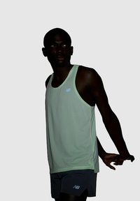 Light green athletic tank top with a breathable texture and a rounded neckline, paired with grey shorts. Features a subtle logo on the chest.