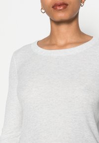 Light grey long-sleeve top, ribbed texture, round neckline, fitted design. No visible patterns or embellishments. Simple and versatile.