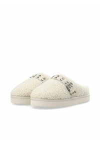 Slip-on hjemmesko i shearling i cremefarve med en tekstureret overflade, prydet med en sølvfarvet rem og dekorative nitter på toppen. Flad sål.