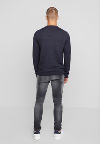 Pull à manches longues marine, encolure ronde, tricot texturé, associé à un jean gris slim-fit et des baskets blanches avec des accents bleus.