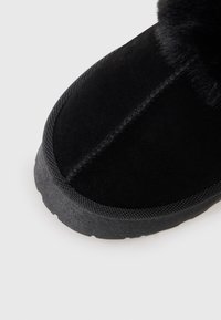 Schwarzer Wildlederstiefel mit einer strukturierten Oberseite, kontrastierender Gummisohle und einem Pelzbesatz am oberen Rand. Verfügt über sichtbare Nähte entlang der Zehen.