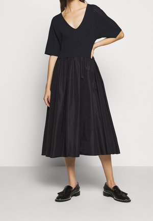 Woman wearing a black V-neck short sleeve top and a black midi skirt paired with black tassel loafers with studded soles.