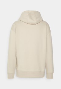 Beige mikina s kapucí vyrobená z měkké, strukturované látky, s volným střihem, žebrovanými manžetami a středovým švem na zadní straně.