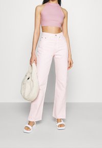 Top corto rosa claro, jeans rosa claro de tiro alto, sandalias blancas y un bolso blanco suave. Tejido suave, corte relajado y diseño de pierna ancha.