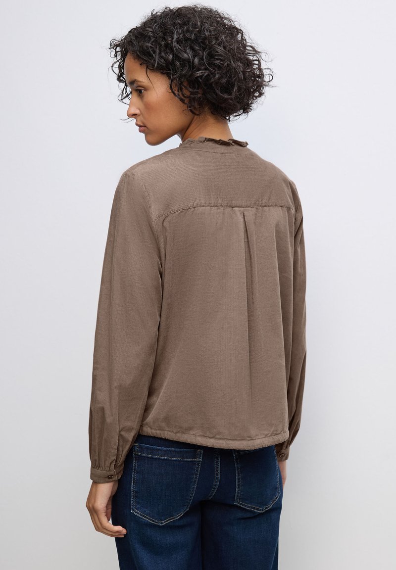 Camicia marrone a maniche lunghe con collo arricciato, texture sottile e pieghetta sul retro, abbinata a jeans blu scuro.