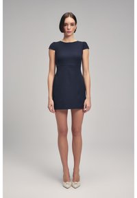 Vestido ajustado de color azul marino con mangas cortas, textura suave, de longitud corta y con una cintura sutilmente estructurada. Combinado con tacones altos beige.