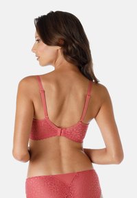 Reggiseno in pizzo di un delicato corallo, con spalline regolabili, chiusura a gancio e motivo floreale. Il retro presenta bordi ondulati per un tocco di dettaglio in più.