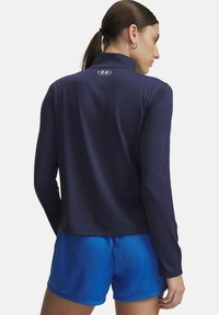 Long-sleeve navy performance top with collar. Features a logo on the back and is paired with blue mesh shorts. Smooth, athletic fit.