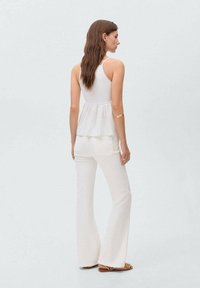 Top peplum blanco con tirantes finos, combinado con pantalones acampanados blancos. Tejido ligero con una textura suave, que muestra un diseño simple sin patrones.