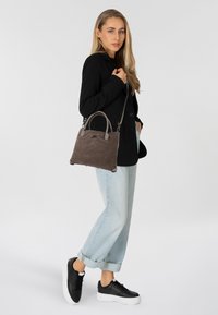 Grijze suède handtas met korte handvatten en een lange verstelbare schouderband. Draag het met een zwarte blazer, lichtblauwe jeans en zwarte sneakers.