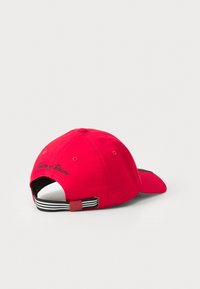 Boné de algodão vermelho com aba curvada, faixa ajustável na parte de trás com riscas pretas e brancas, e texto bordado discreto na parte de trás.