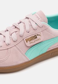 Baskets en daim rose avec accents turquoise, dotées d'un patch logo doré, de lacets plats et d'une semelle en caoutchouc texturée.