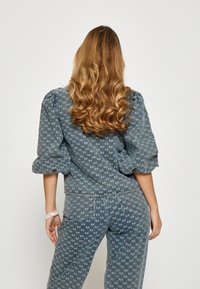 Denimowy strój w stonowanym niebieskim kolorze z geometrycznym wzorem. Top z bufiastymi rękawami; spodnie mają tylne kieszenie i zwężany krój. Widoczne detale przeszycia.