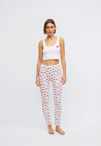 Crop top blanc avec un motif de cerise, associé à des leggings blancs ornés d'un motif de cerises rouges. Matière en coton doux et extensible.