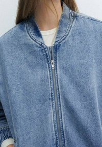 Denim bomberjack in lichtblauw, met een rits aan de voorkant, ronde kraag en een textuur met subtiele vervagingdetails.