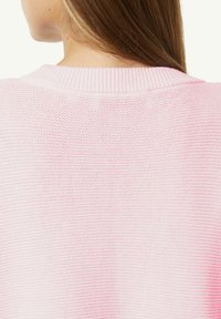 Jasnoróżowy sweter spacerowy z dzianiny, z żeberkowym dekoltem i teksturowanym materiałem. Widok z tyłu podkreśla całkowitą miękkość tkaniny.