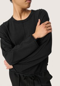 Black long-sleeve sweatshirt with a round neckline and relaxed fit. Features ribbed cuffs and hem, with a smooth texture and casual design.