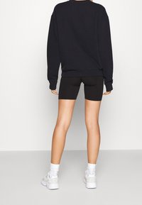 Svart oversized sweatshirt med lång ärm, parat med svarta cykelshorts. Vita sneakers fulländar outfiten, vilket visar en avslappnad sportig look.