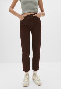 Pantaloni din bumbac maron cu croială dreaptă, talie �înaltă și buzunare frontale, asortați cu adidași de culoare deschisă și șosete crem.