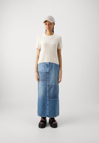 Beiges, gestricktes Oberteil mit kurzen Ärmeln, blaue Jeans-Maxi-Rock mit Patchwork-Design und schwarze Plattform-Ankle-Boots. Hellfarbige Mütze.