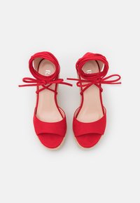 Sandali espadrilles in suede rosso con lacci alla caviglia, dotati di una ampia fascia frontale e una suola in corda di juta testurizzata. Sottopiede in tinta unita visibile.
