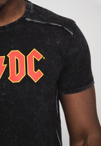 Black t-shirt featuring a distressed texture, round neckline, short sleeves, and a prominent red and yellow "AC/DC" graphic on the front.