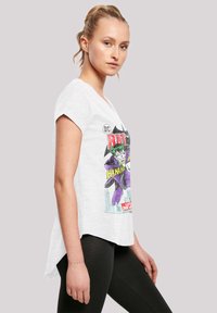 Hvit grafisk T-skjorte med trykk av en skurk, med korte ermer og buet kant. Brukt sammen med svarte leggings.