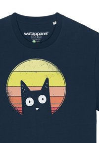 Un t-shirt bleu marine présente un design graphique d'un chat noir sur un dégradé circulaire de coucher de soleil comprenant des teintes de jaune, d'orange et de rose.