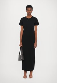 Rochie maxi din bumbac negru, cu mâneci scurte, având fante laterale și o croială lejeră. Complementează look-ul cu o poșetă mică gri și sandale nude.