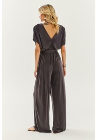 Sivý overal so širokými nohavicami, uzlom v páse, krátkymi dolman rukávmi a dizajnom s V-výstrihom na chrbte. Hladká textura; ležérny silueta.