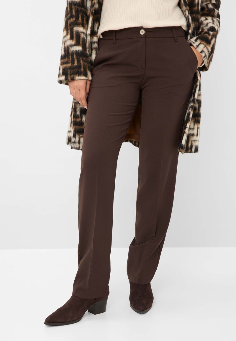 Personne portant un pantalon droit marron foncé, un pull beige côtelé, un manteau à motifs marron et blanc, ainsi que des bottines à talons marron foncé.