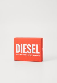 Piros téglalap alakú doboz fehér, vastag betűkkel "DIESEL" felirattal, és kisebb szöveggel "A SIKERES ÉLETÉRT" egy sima fehér háttér előtt.