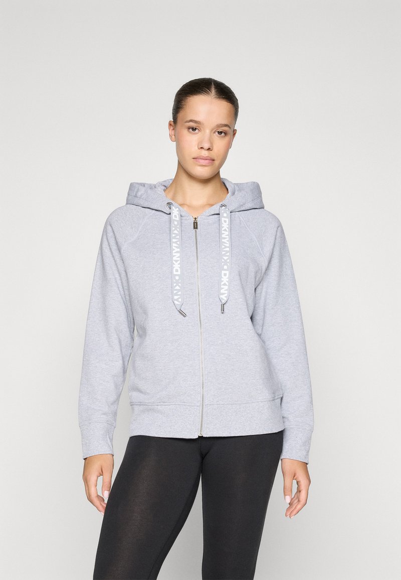 Sweatshirt cinza com fecho e capuz, apresentando cordões em contraste e punhos canelados. Mostrado com leggings pretas, textura suave.