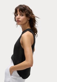 Top de punto negro sin mangas con un acabado texturizado, escote redondo y corte relajado, combinado con pantalones blancos.