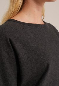 Suéter gris oscuro hecho de material de punto suave, con un cuello redondo y una textura lisa, y un patrón sutil y uniforme en toda su superficie.