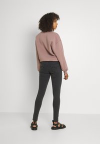 Sweatshirt oversized rosa claro com punhos canelados, combinado com calças skinny cinza escuro com bolsos traseiros e sandálias pretas.