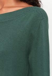 Green knit sweater with a wide, ribbed neckline and soft texture. Features a relaxed fit and slightly tapered sleeves.