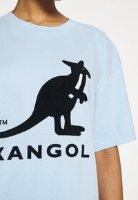 Camiseta de algodón azul claro con un gran gráfico de un canguro negro y la palabra "KANGOL" en texto negro en negrita debajo del diseño.