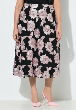 Schwarzer Midirock mit großer hellrosa Blumenstickerei, getragen mit rosa Slingback-Pumps auf hellem Hintergrund.